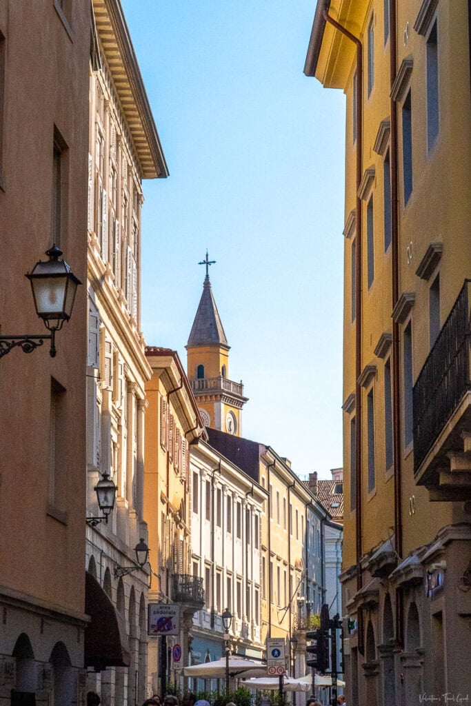 "Narrow street in Trieste's old town with historic buildings and a church tower in the background, highlighting that Hotel Capitelli is the perfect hotel in Trieste for families, and one of the Trieste hotels close to the Trieste ship port terminal."
