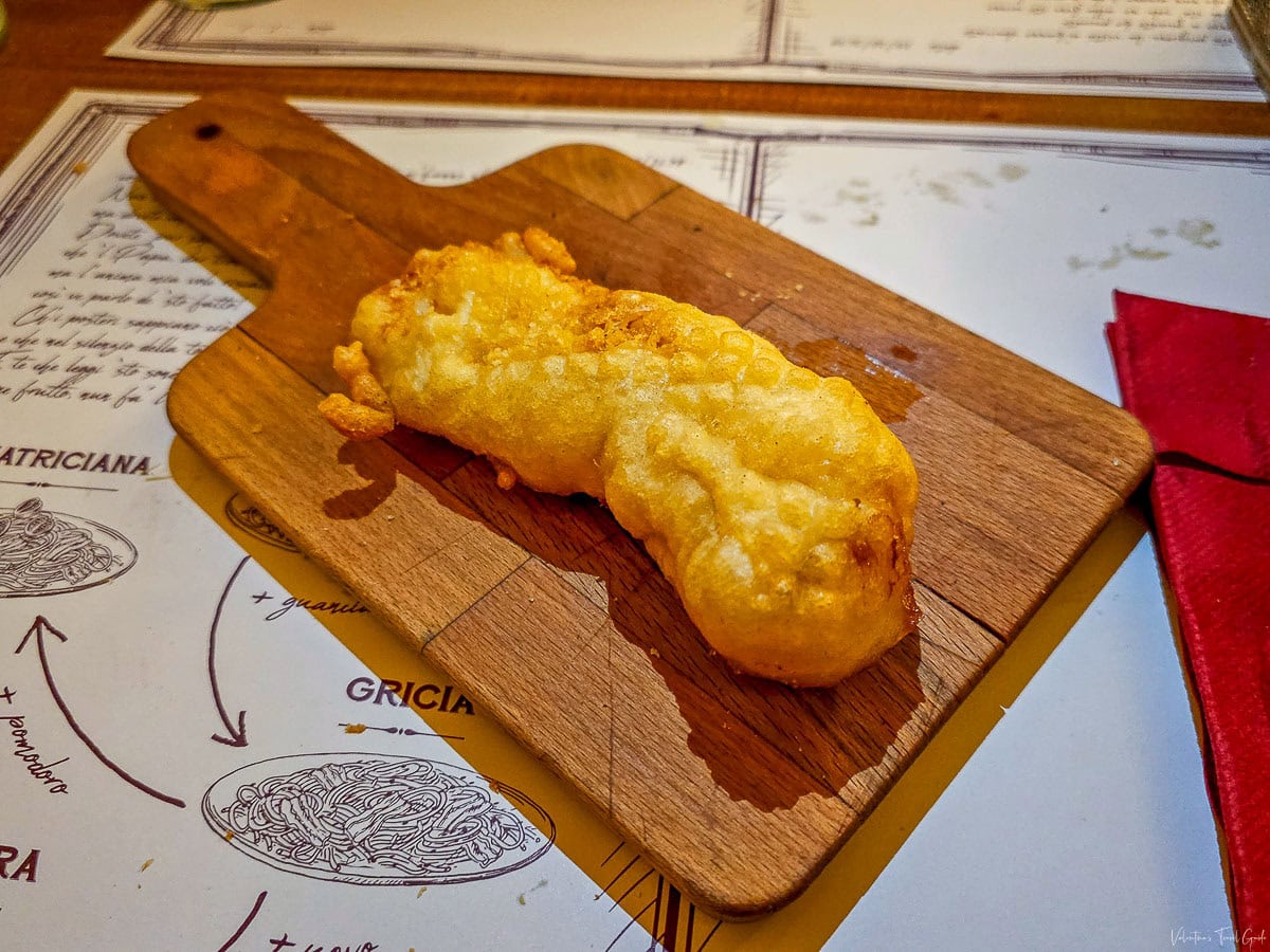 Golden fried cod (baccalà fritto) served on a wooden board at La Gattabuia restaurant, a top choice for traditional dishes at one of the best fish restaurants in Rome