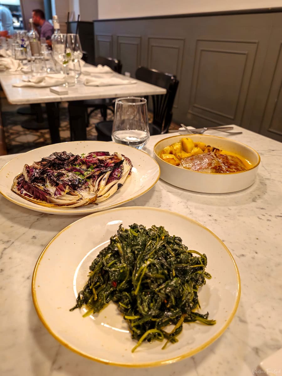Plated dishes featuring sautéed chicory, grilled radicchio, and a classic Roman meat dish at a restaurant near Piazza Navona, showcasing authentic local cuisine in an elegant dining setting
