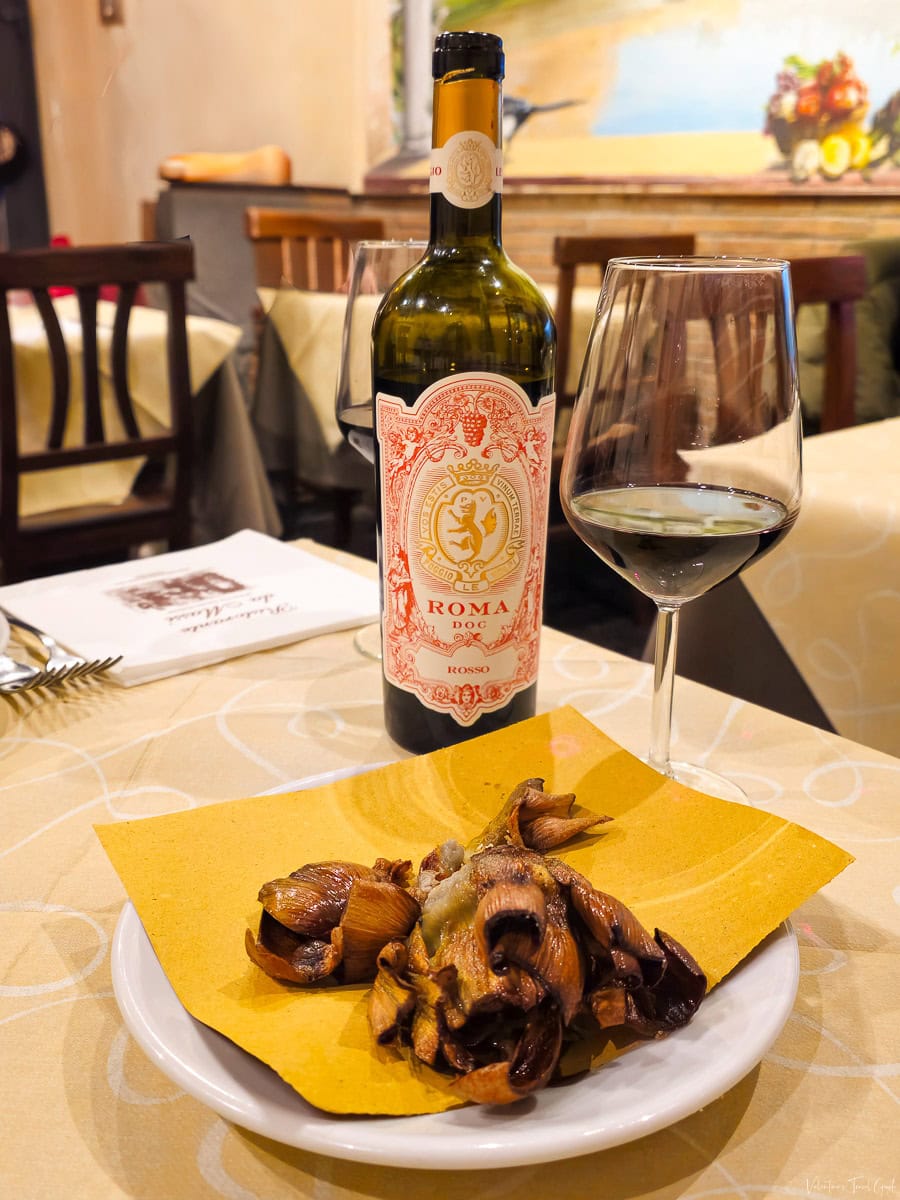 Plate of crispy fried artichokes (Carciofi alla Giudia) served with a bottle of Roma DOC red wine, capturing the authentic flavors at one of the traditional restaurants