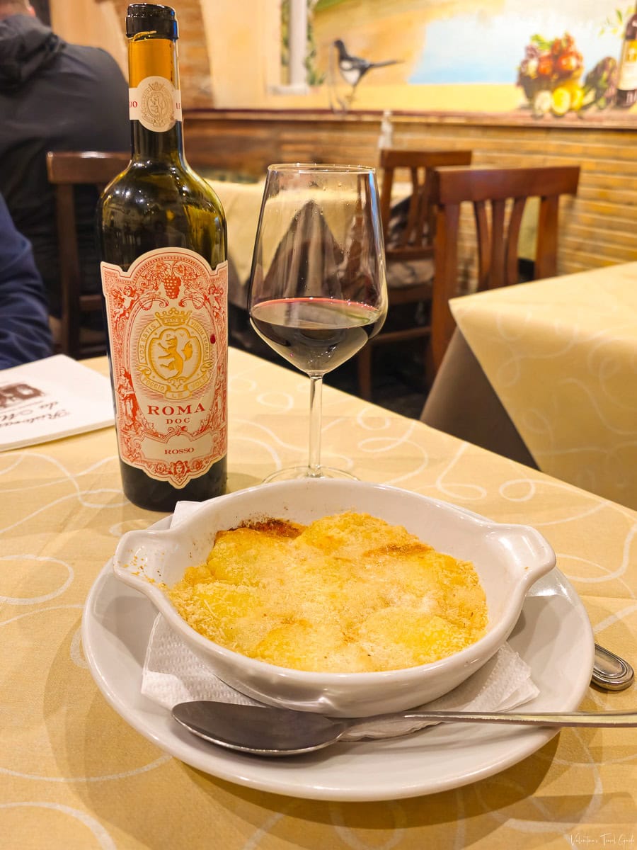 Plate of golden, baked gnocchi alla romana served with a glass of red wine and a bottle of Roma DOC at Ristorante da Massi, exemplifying the authentic cuisine and cozy atmosphere of where to eat in rome like a local
