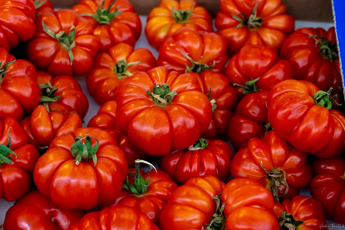 A vibrant display of plump, red heirloom tomatoes at a market in Rome, showcasing one of the fresh ingredients central to Italian cuisine. These tomatoes' often used in iconic dishes in Rome like Amatriciana and Pomodoro sauces, celebrated for their rich flavor and culinary versatility.
