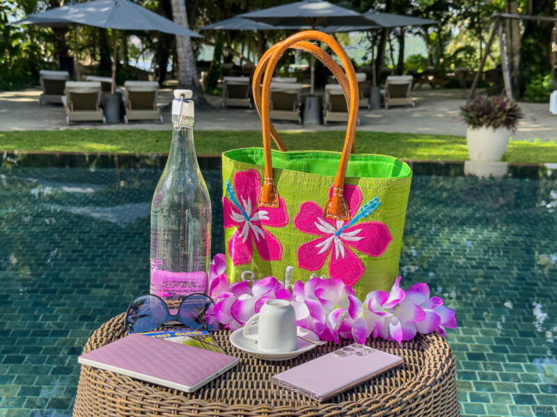 summer vacation bag checklist a green and pink beach bag with a bottle of water, an e-reader, a sunglasses, a phone and a cup of espresso