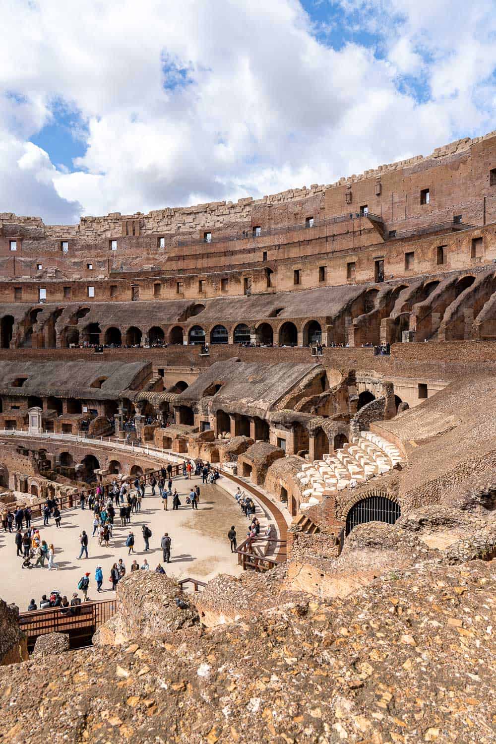 Interior view of the Colosseum in Rome showing multiple levels of ancient stone seating and a crowd of tourists exploring the arena floor. Highlights the scale and preserved structure visitors experience when visiting Colosseum in Rome.